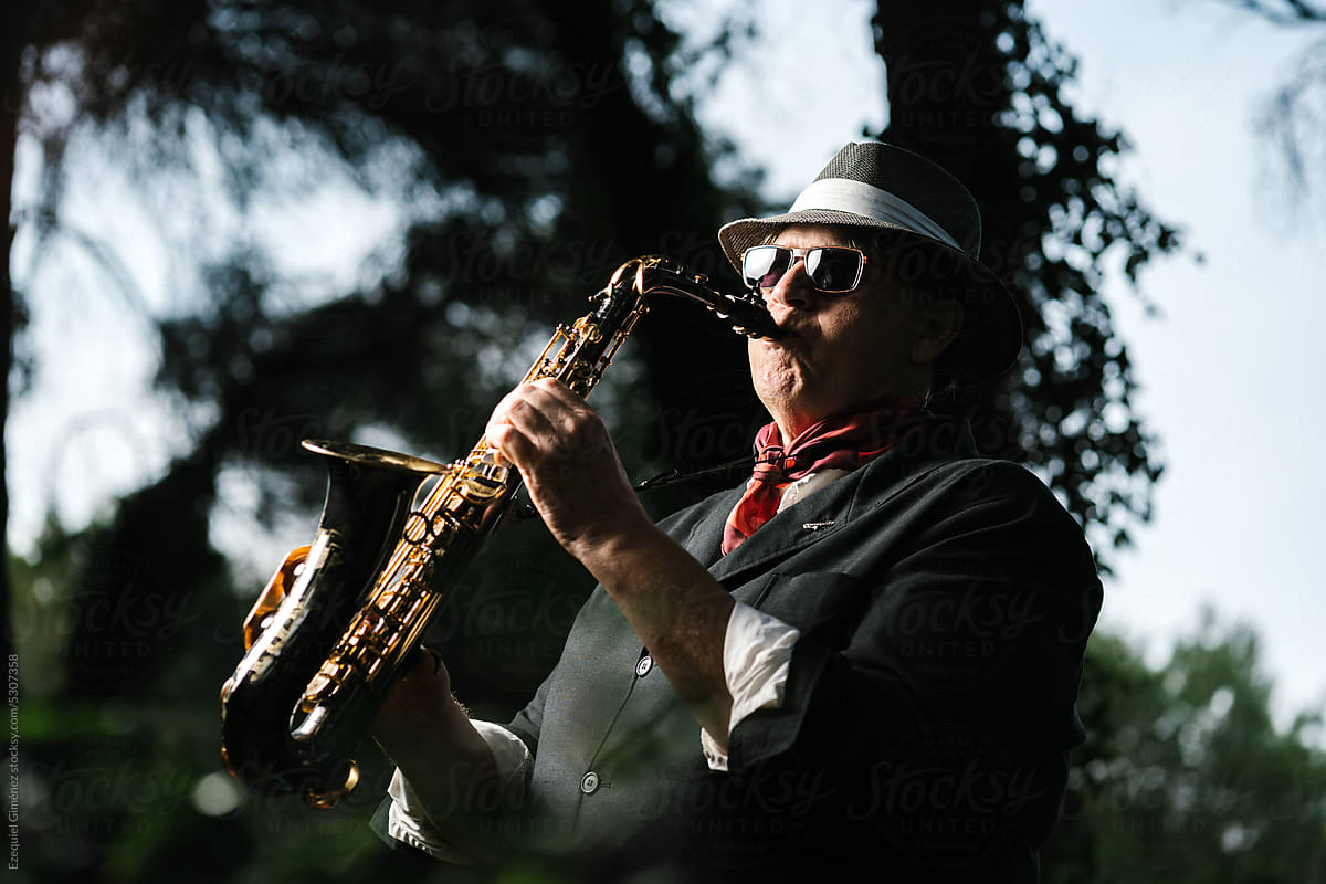 Male artist playing saxophone in park on summer day