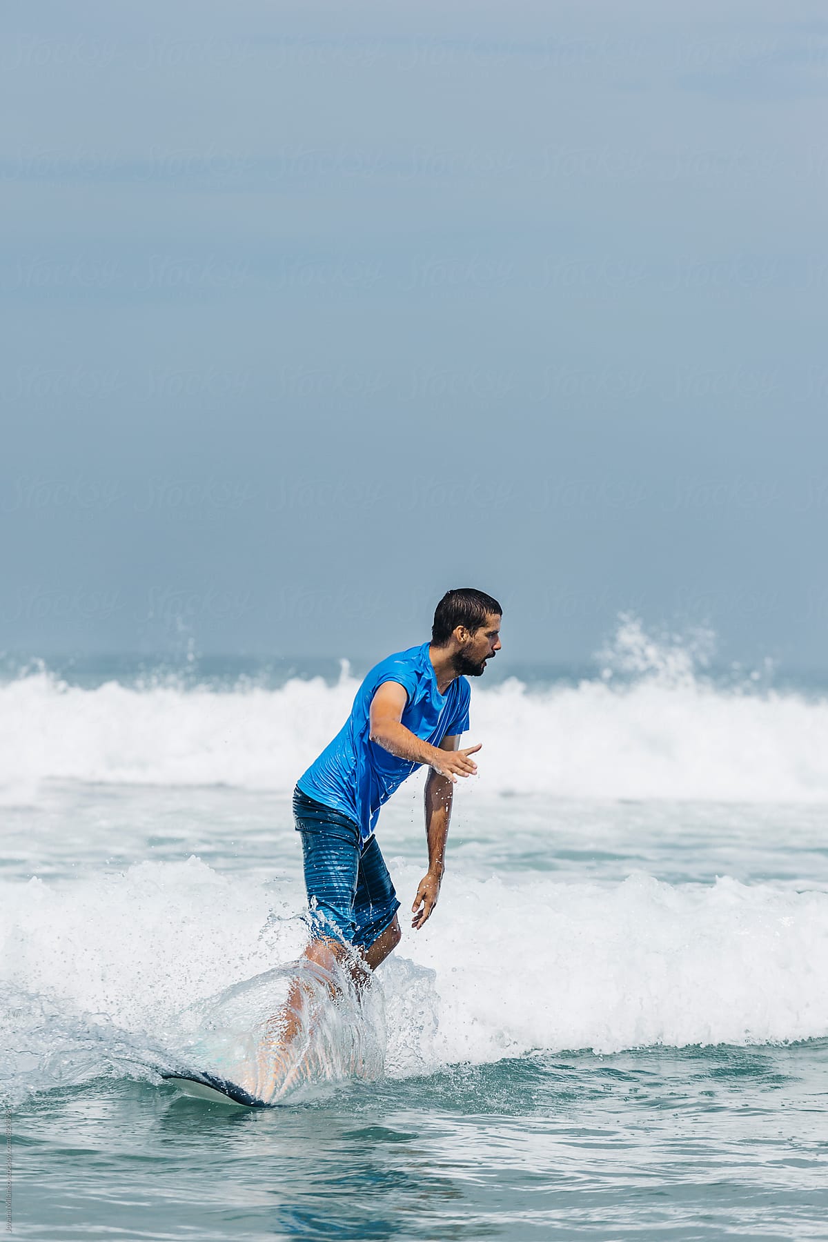 Young man learning to surf the waves on long surfboard