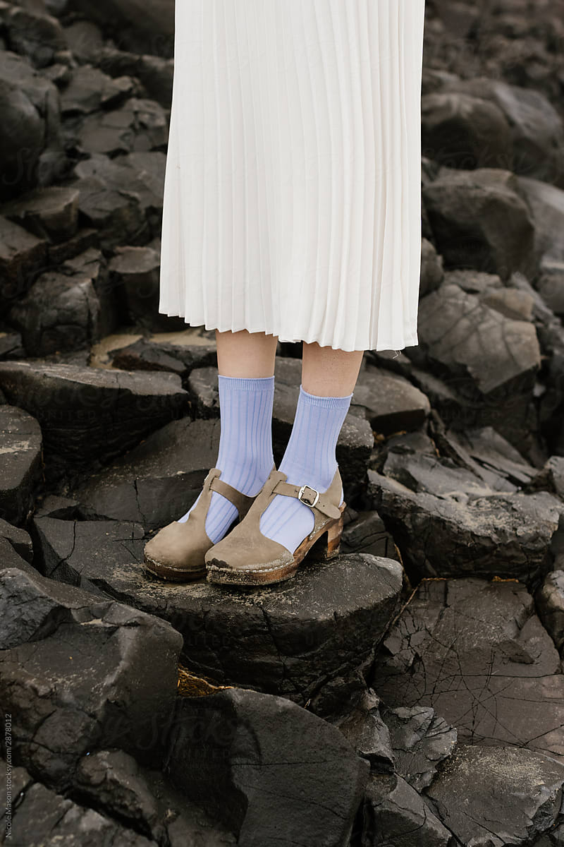 person standing in long white skirt on dark rocks with colored socks