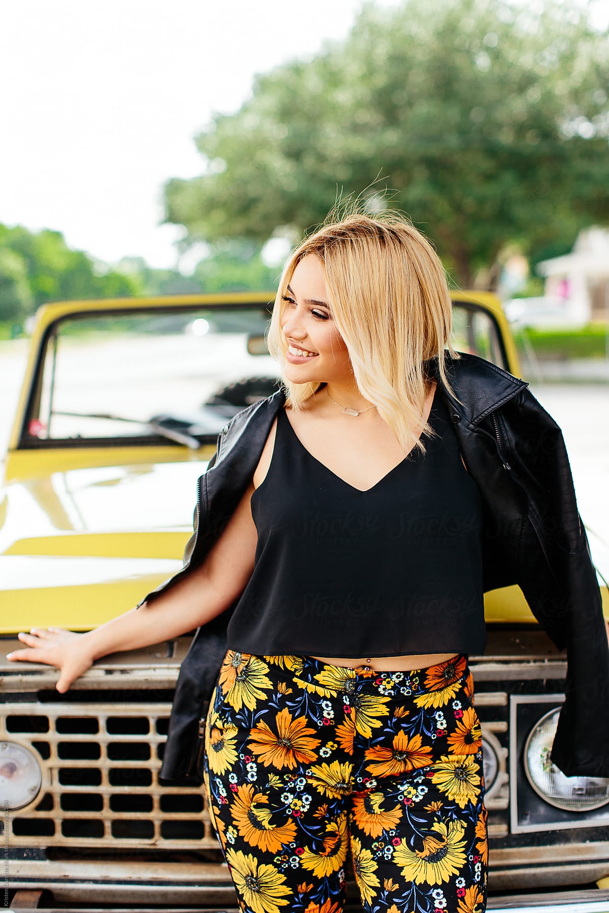 A beautiful woman leaning up against a yellow car.