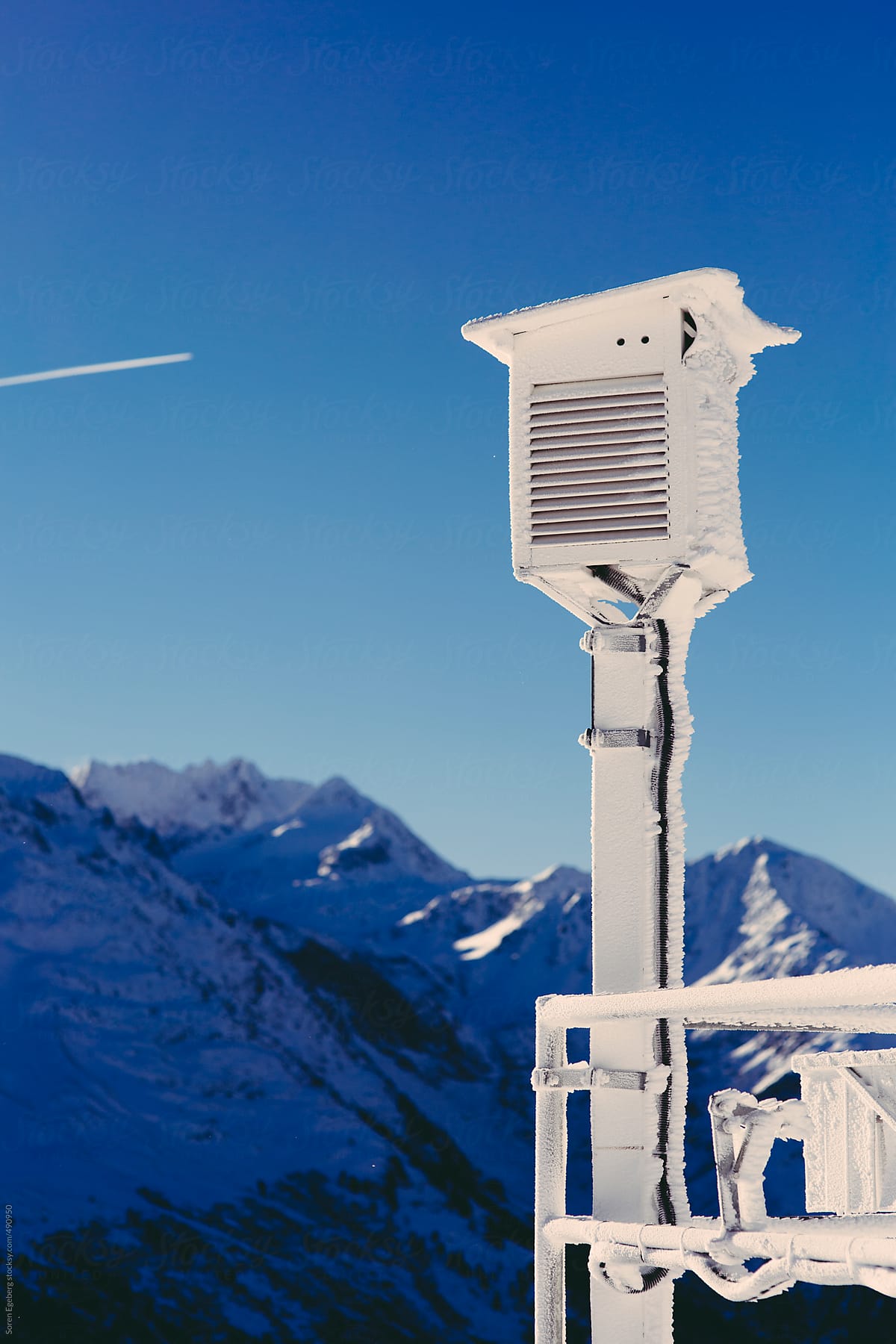Weather station in the mountains against a blue sky in winter with flight trails and copyspace