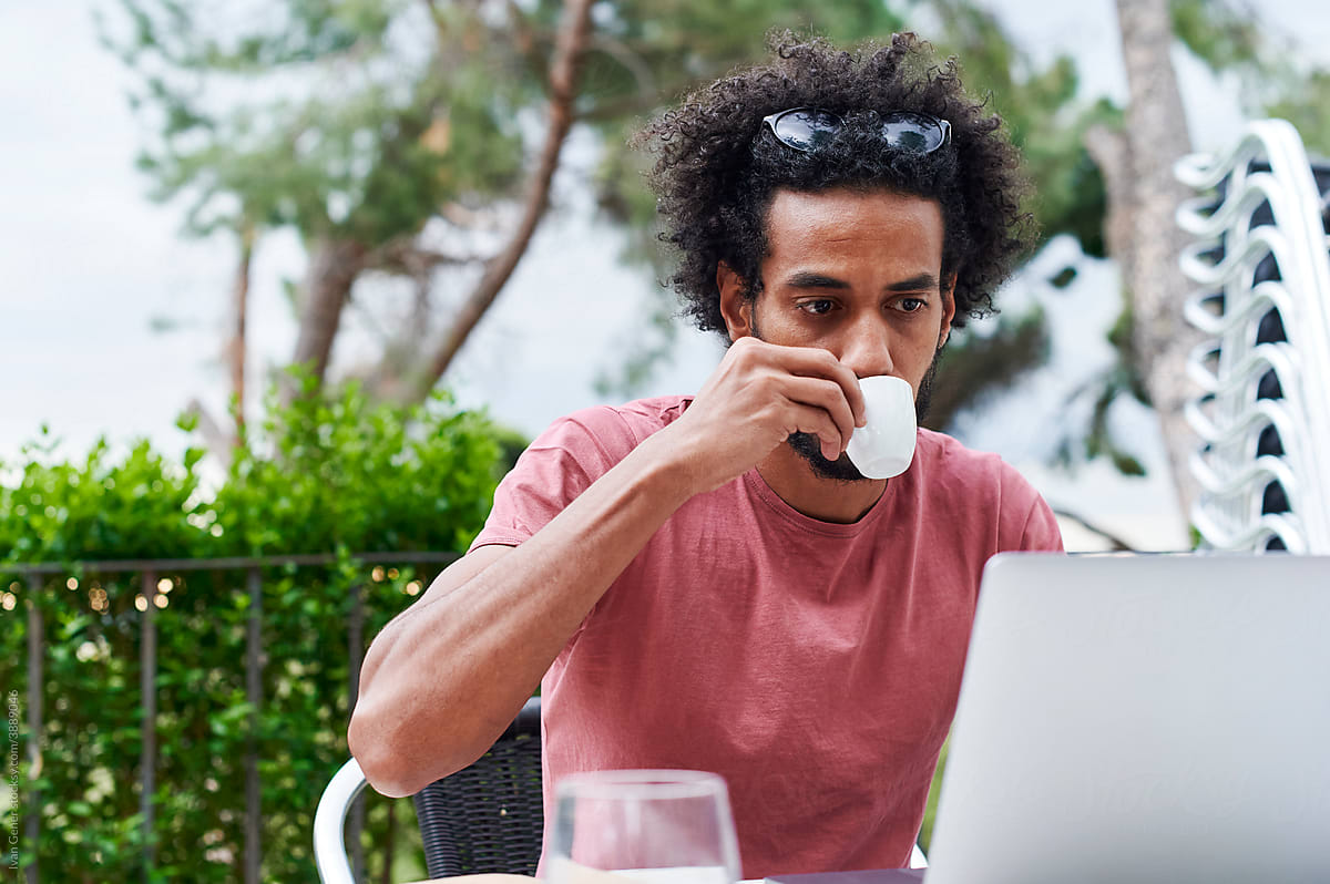 Man using a laptop over coffee at a sidewalk cafe