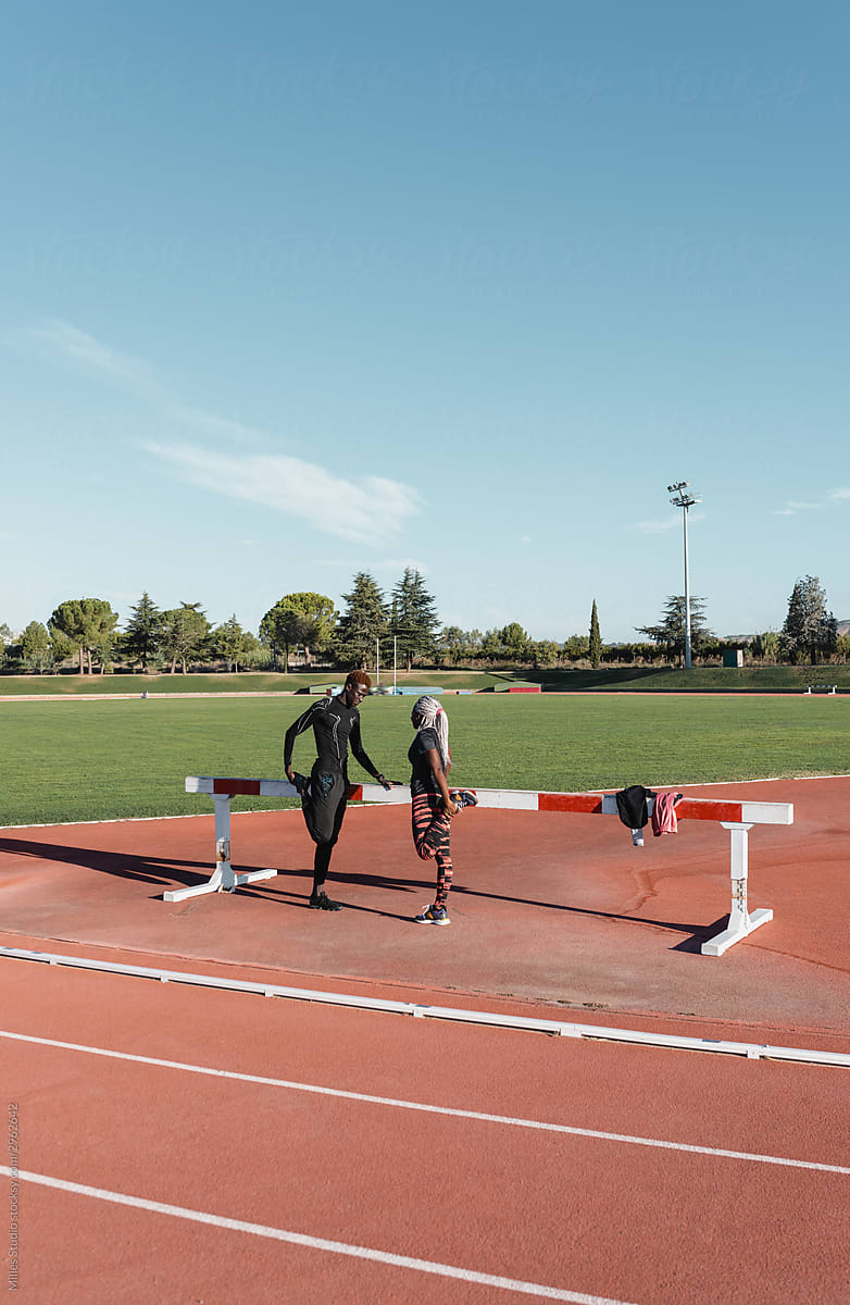 Black sportsman and sportswoman stretching legs near barrier