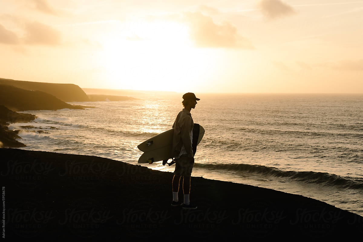 A backlit portrait captures a young surfer searching for the high tide