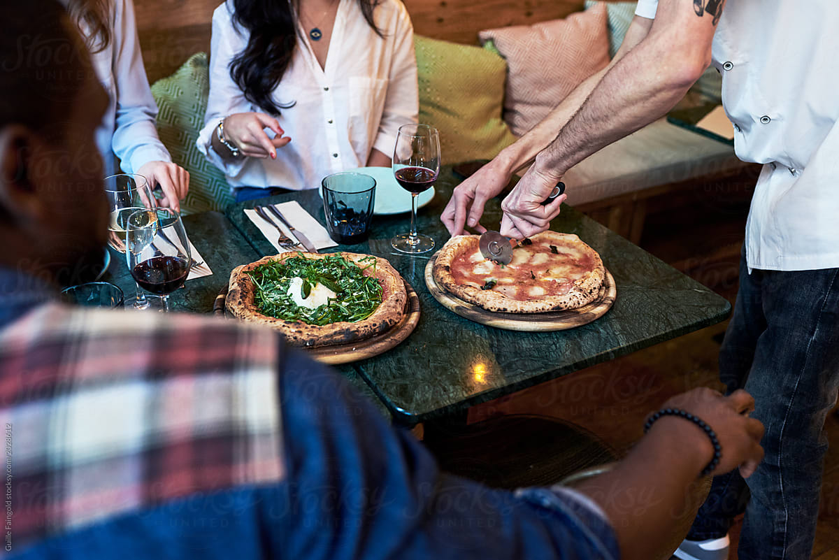 Waiter cutting pizza with knife on table in front