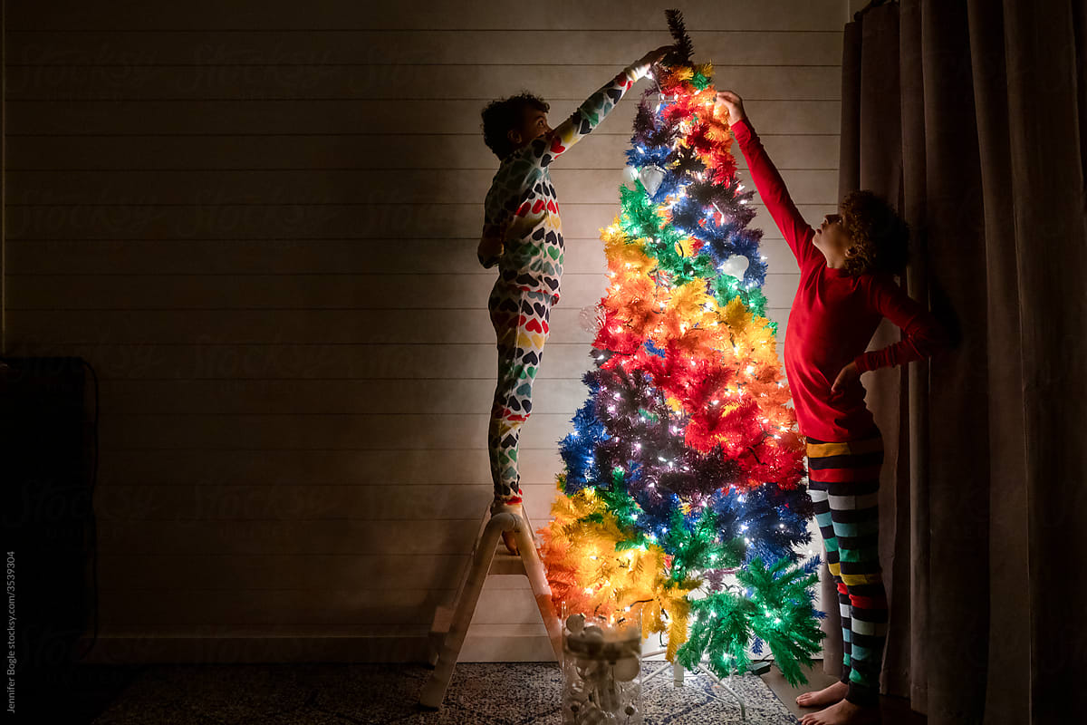 Siblings decorate a rainbow Christmas tree