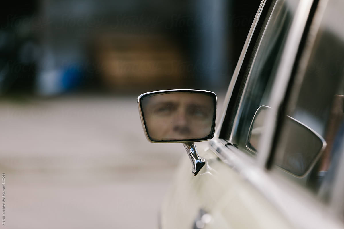 face part of young man in old car mirror
