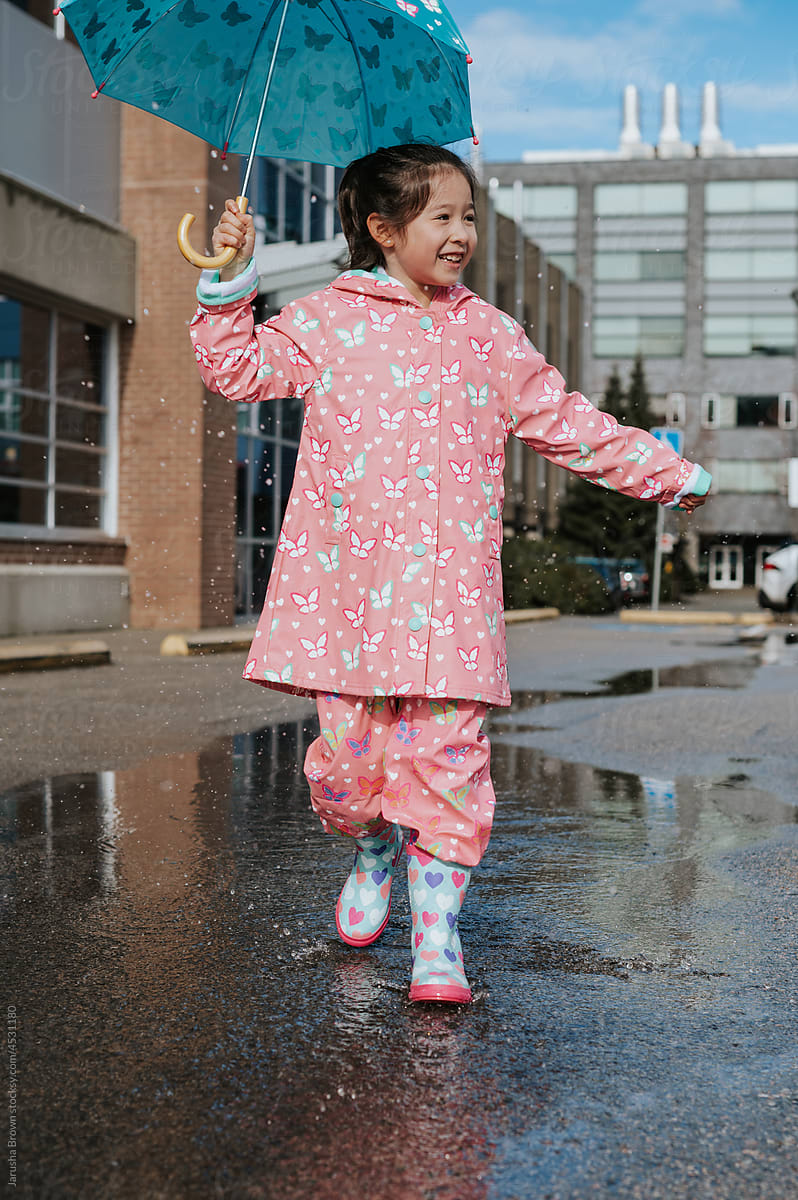 Young girl walks in a puddle with rain boots and an umbrella.