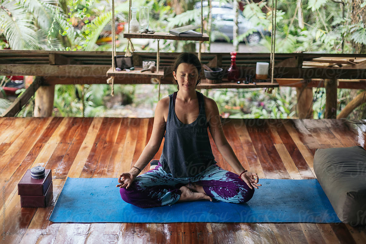 Woman doing yoga and meditating on wooden floor of an outdoor terrace