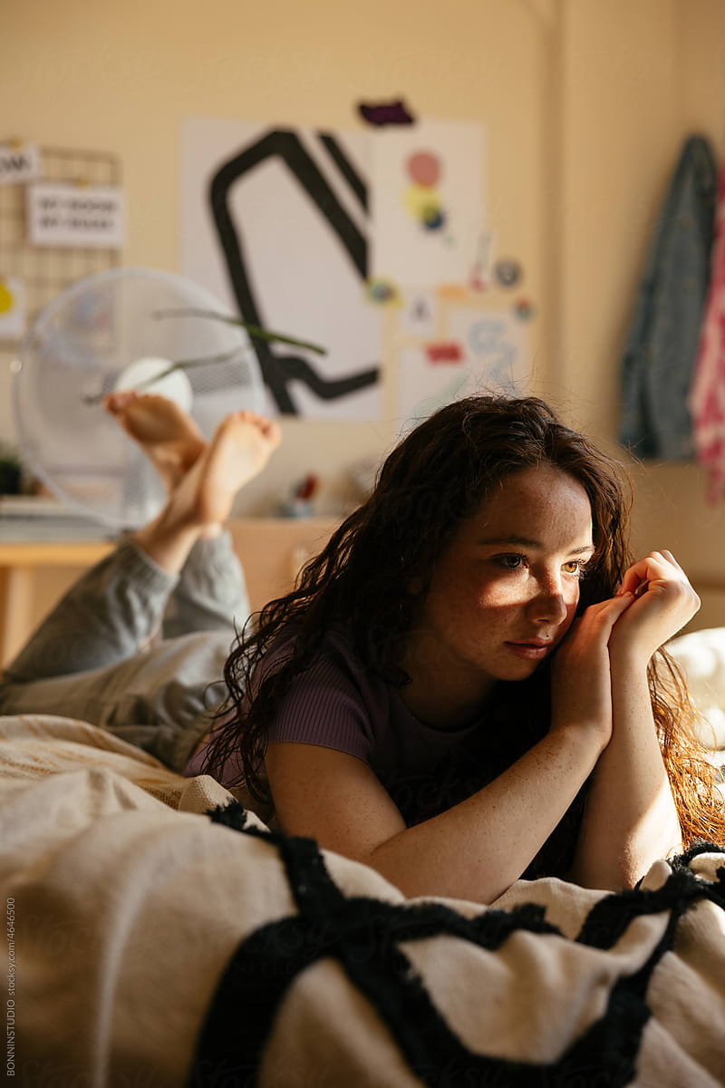 Freckled teen girl resting on bed in own room