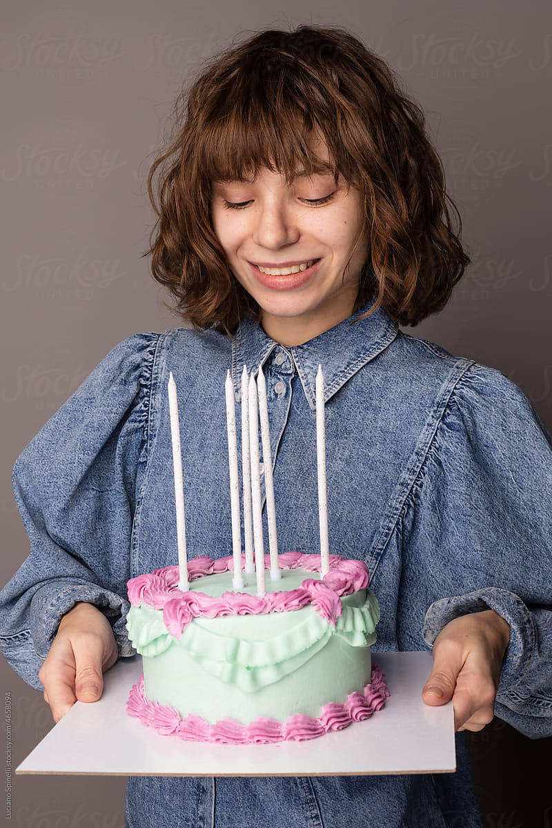 Happy curly girl in a blue shirt smiling and holding a pastel cake