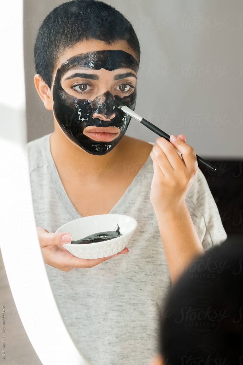 Ethnic female applying black mask in front of mirror
