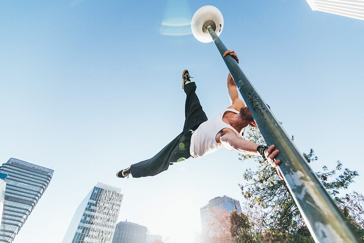 Man holding on to lamp post in mid air during a parkour training