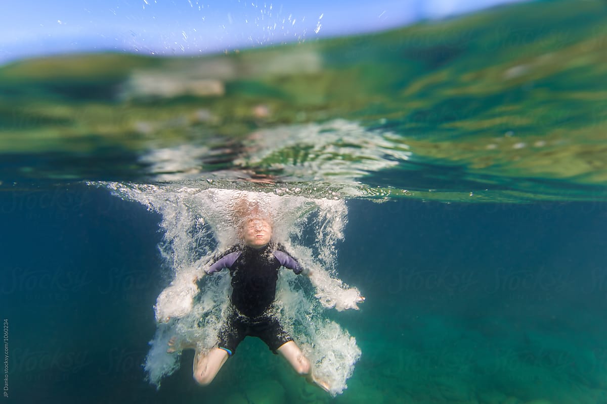 Underwater Splash and Bubbles of Boy Jumping Into Summer Lake From Water Trampoline At Cottage
