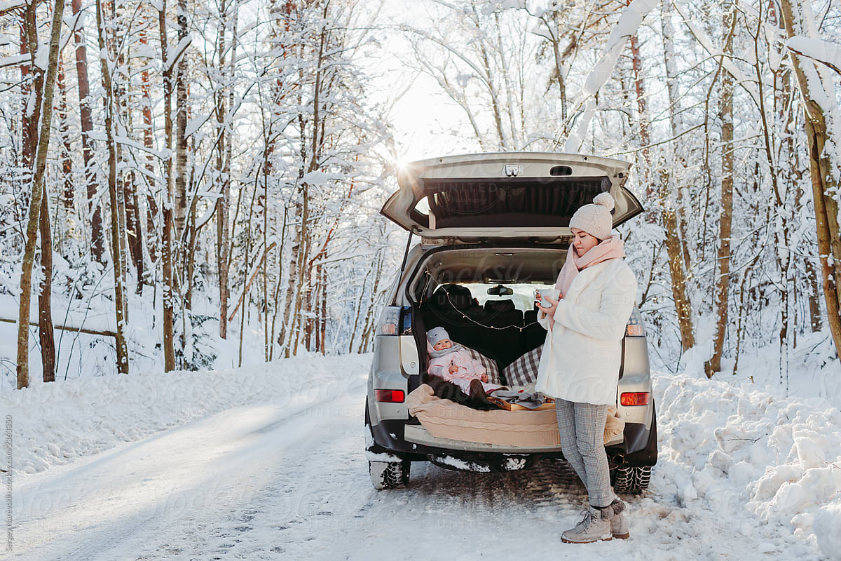 Mother near car and baby in car trunk in winter forest