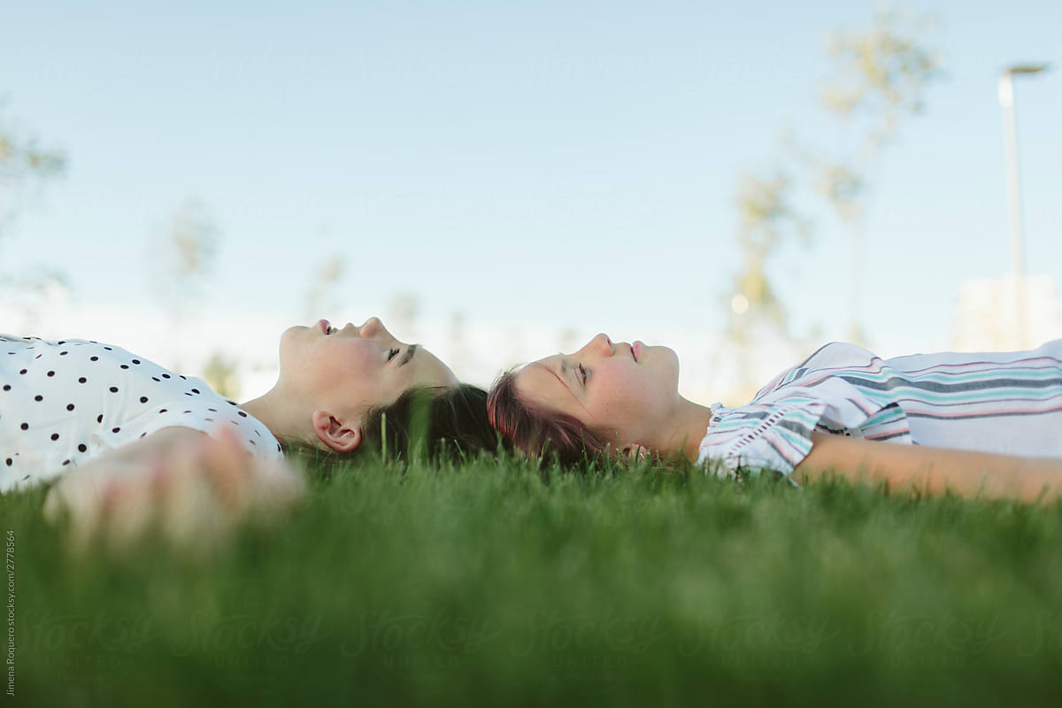 Two teenage girls head to head lying on the grass.