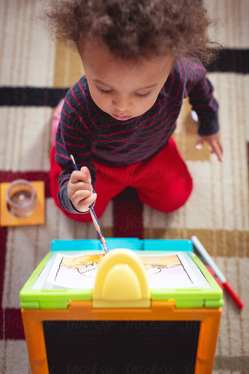 Toddler child painting happily on a toy easel