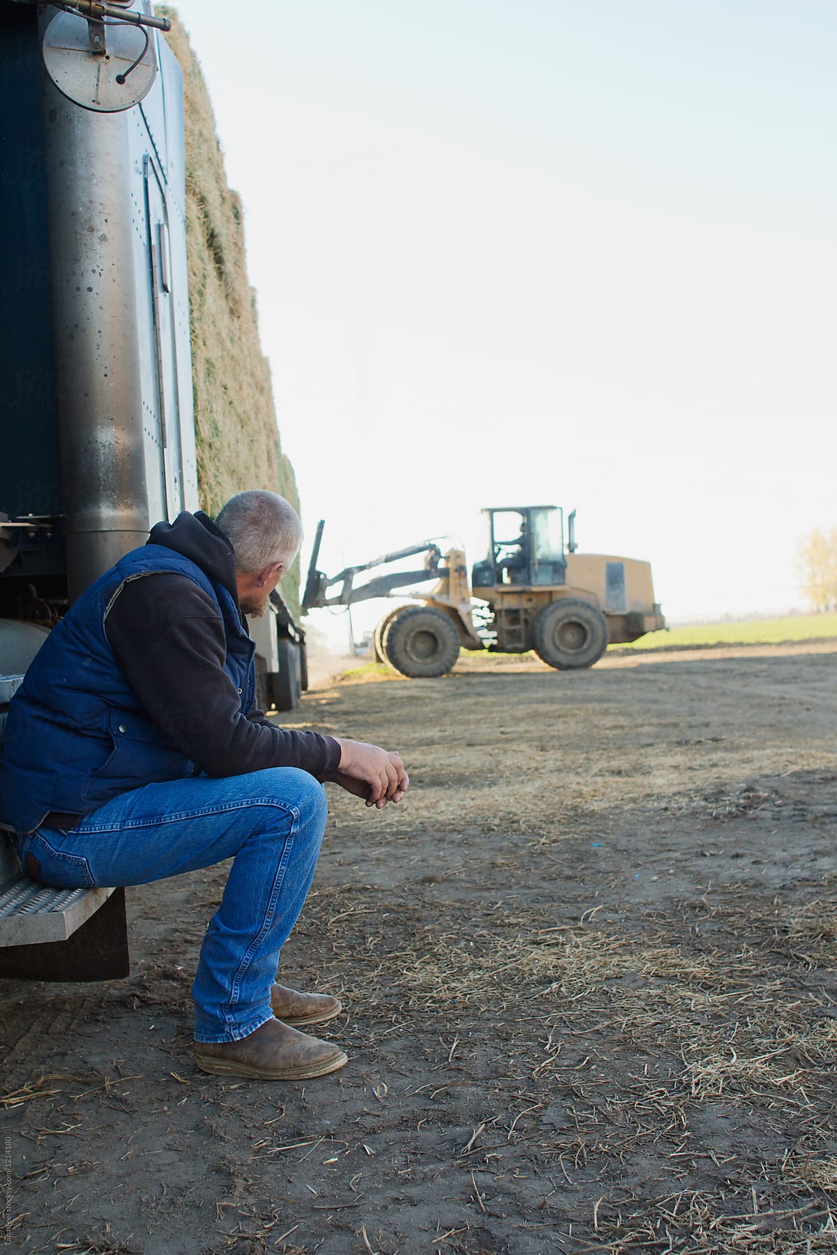 driver sits and waits for loader to unload hay