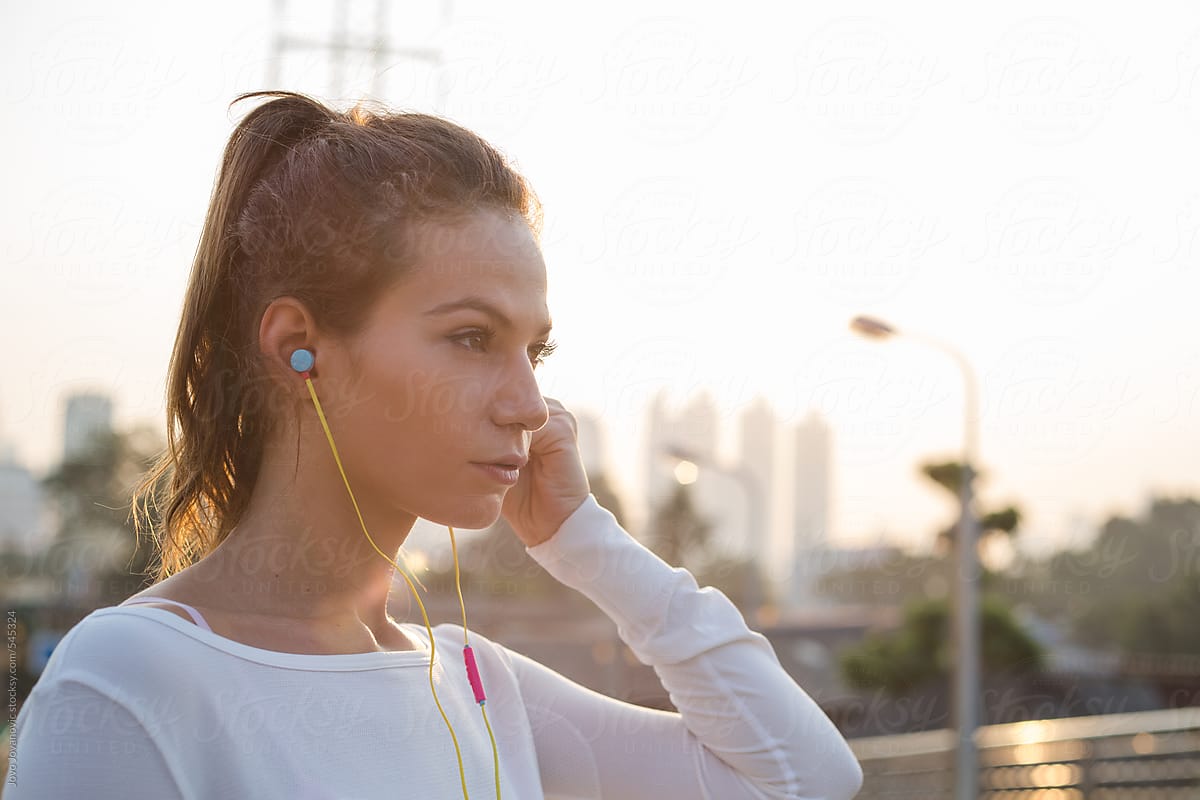 Young beautiful woman with headphones jogging and listening music in street