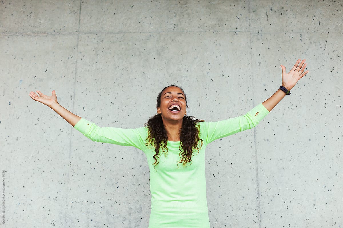 Young african american woman laughing with arms wide open in front a wall.
