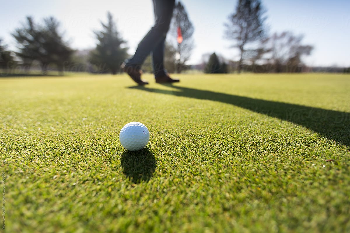 Golf ball on course putting green with person walking