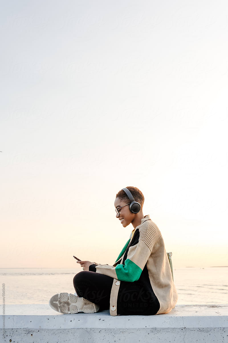 Woman with headphones and smartphone sitting at embankment