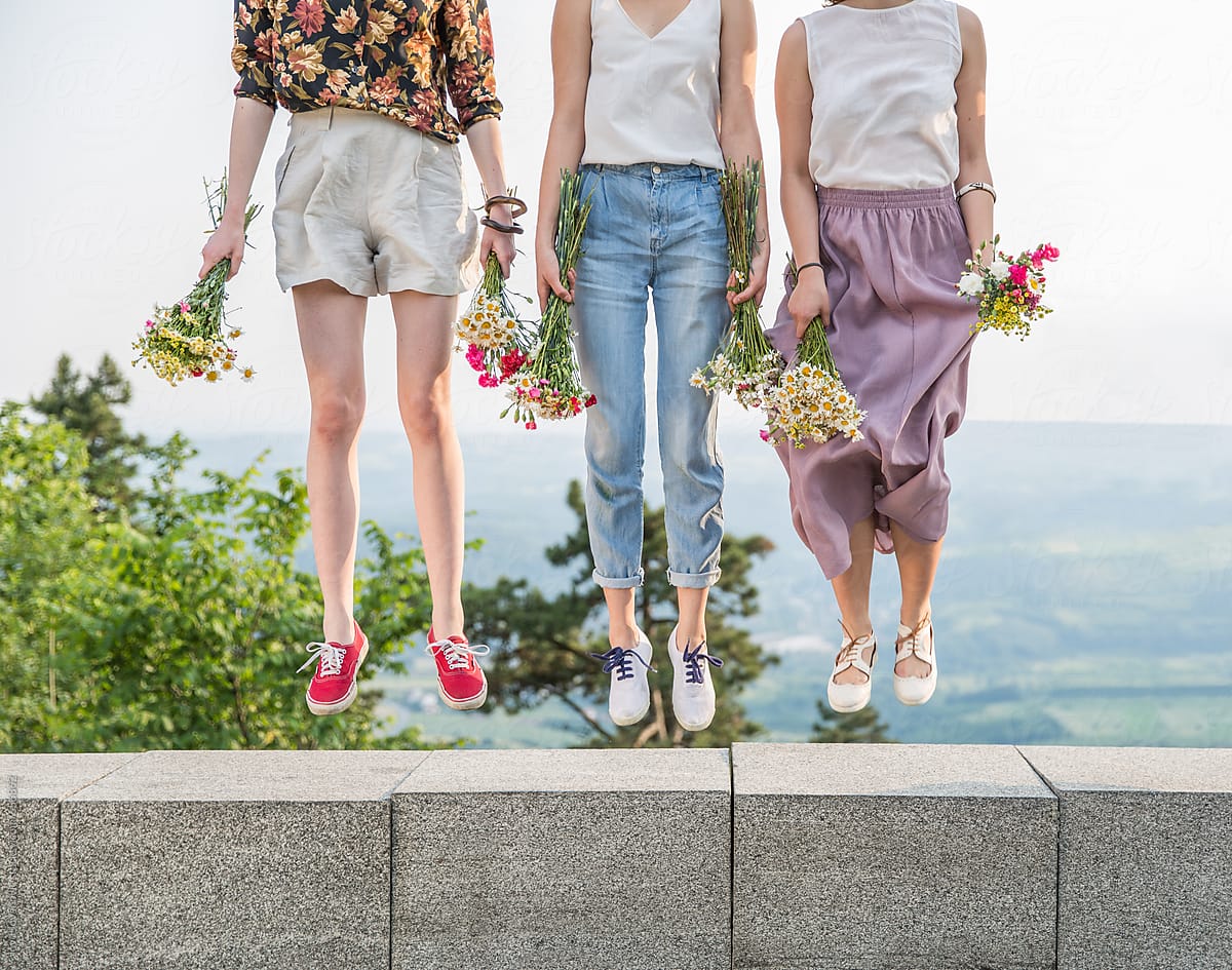 Three girlfriends levitating while holding flowers, spring season