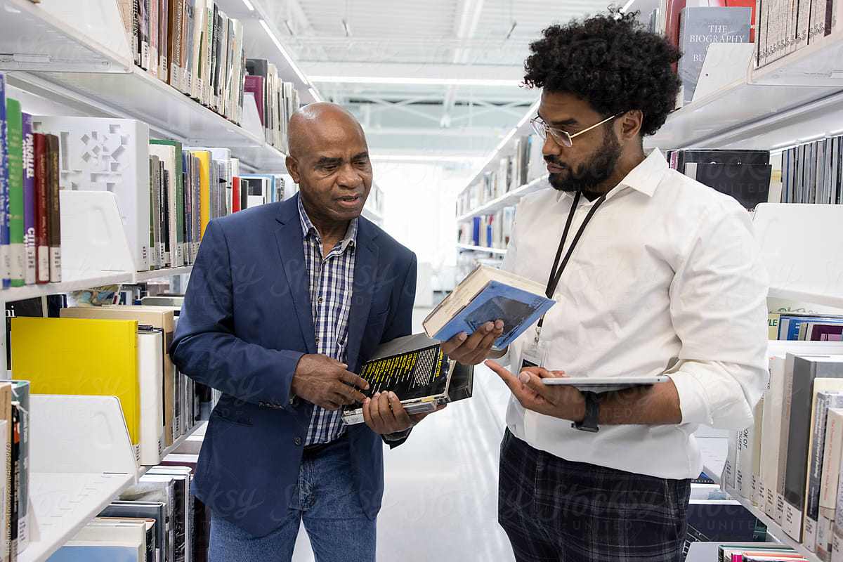 Librarian helping man with books in library aisle.