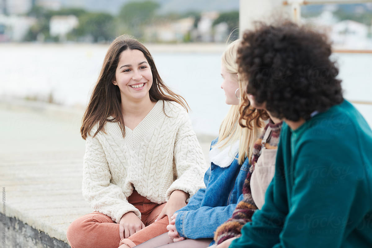 Brunette girl sitting on pier of lake with her friends.