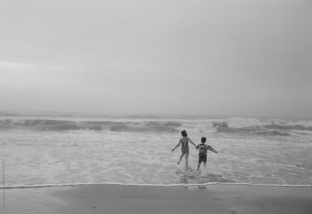 Black and white photo of two children running into an ocean