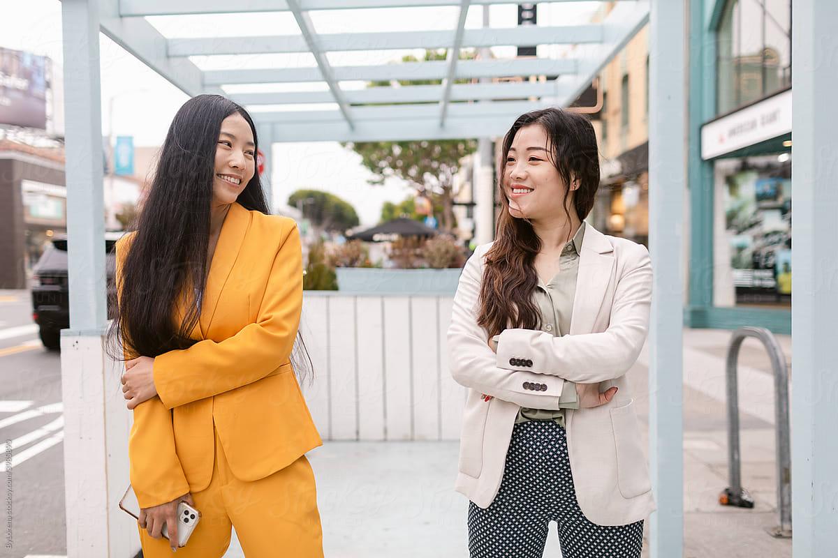 Trendy Chinese girlfriends looking at each other on street