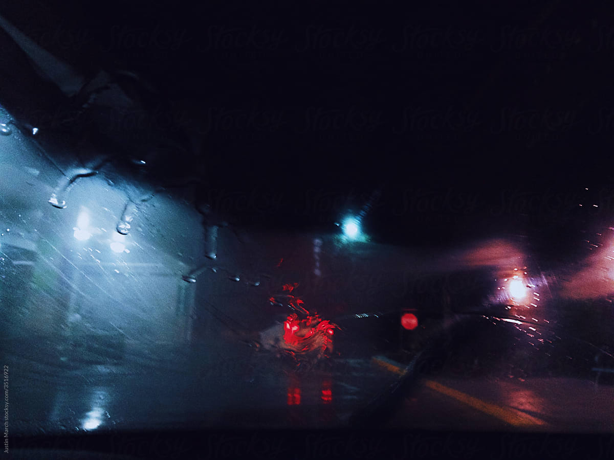 street scene shot in the rain at night through the windshield featuring a car with their break lights on.