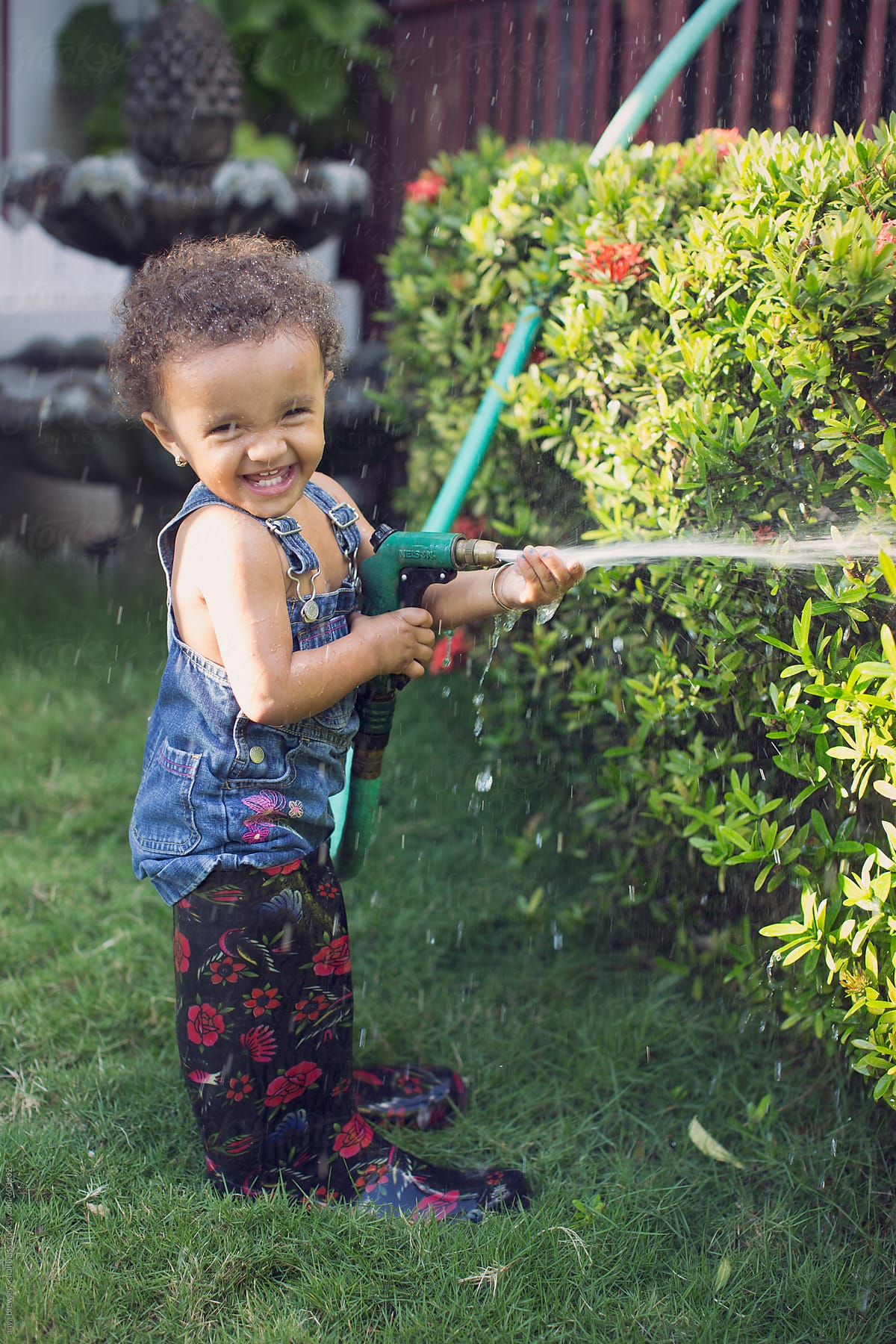 A  toddler child in galoshes playing with a garden hose