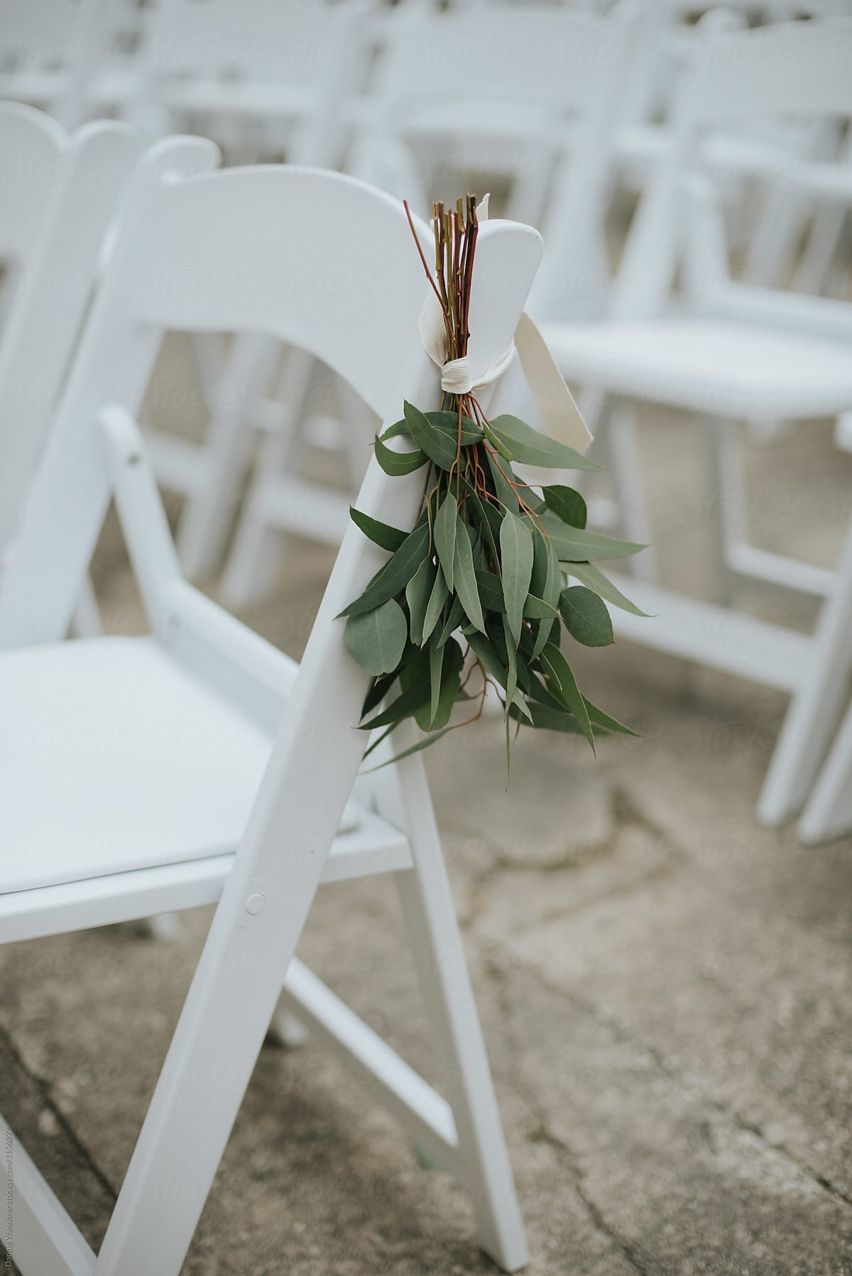 Simple greenery details on white chairs for wedding ceremony