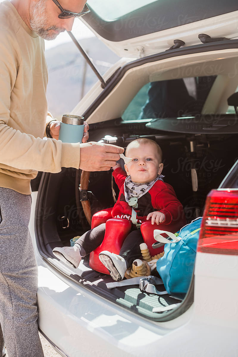Father feeding cute baby in car trunk