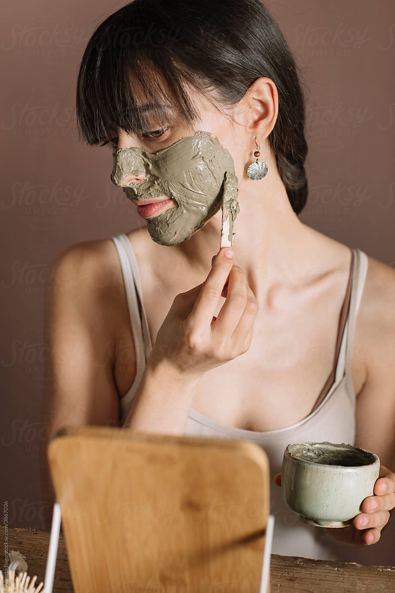 Young Woman Applying Green Clay Mask On Her Face