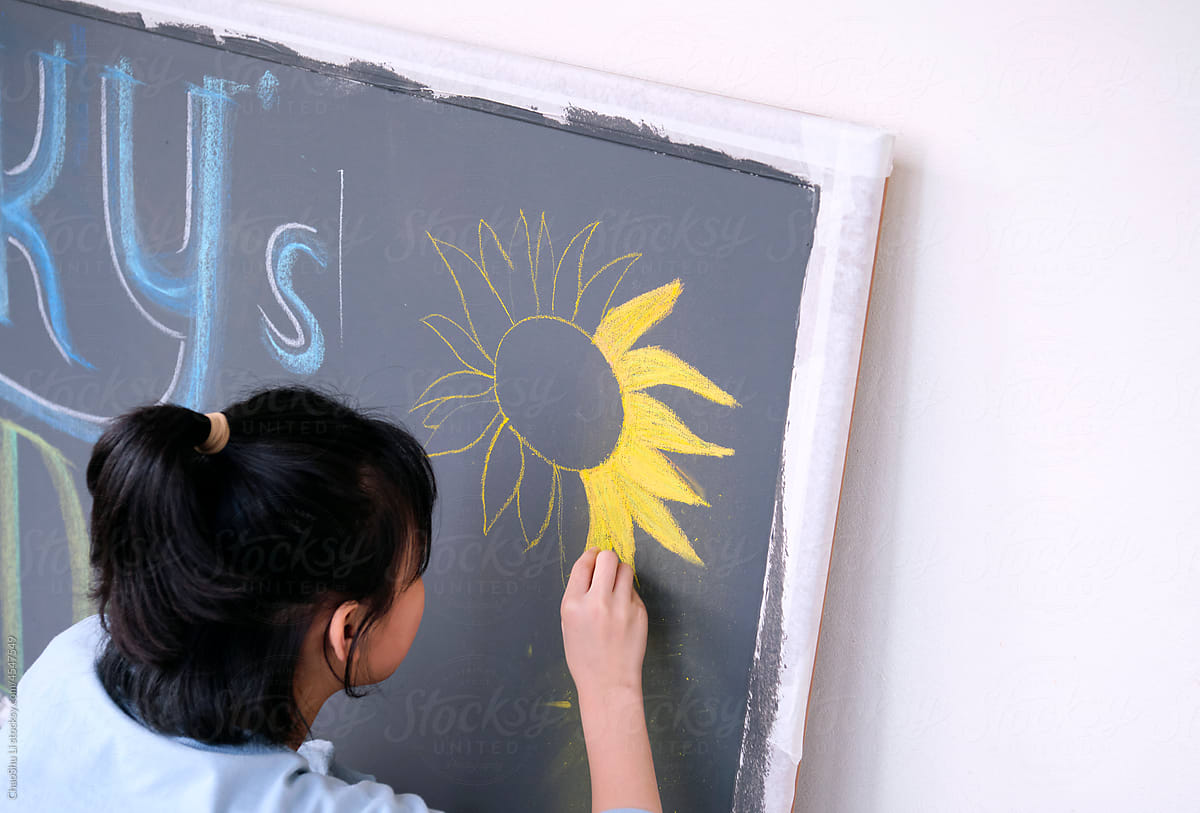 Closeup little asian girl creating chalk drawing on blackboard