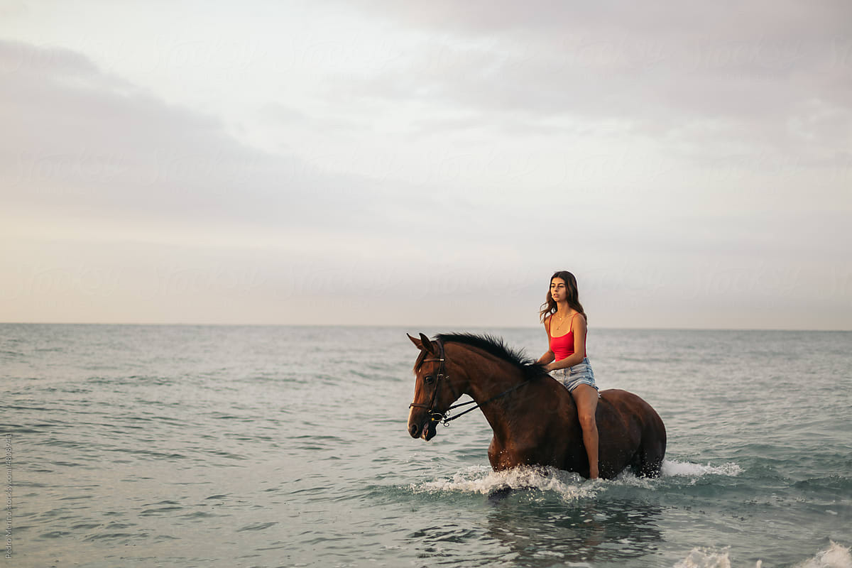 Young woman riding a horse into the sea