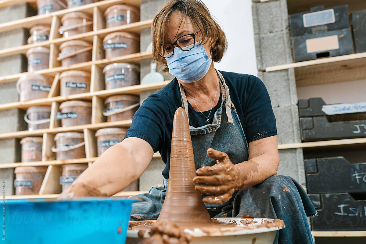Mature craftswoman pouring water on the clay in the workshop