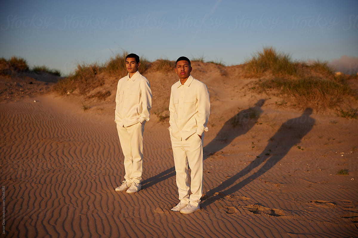 Stylish male models in white outfits standing in desert