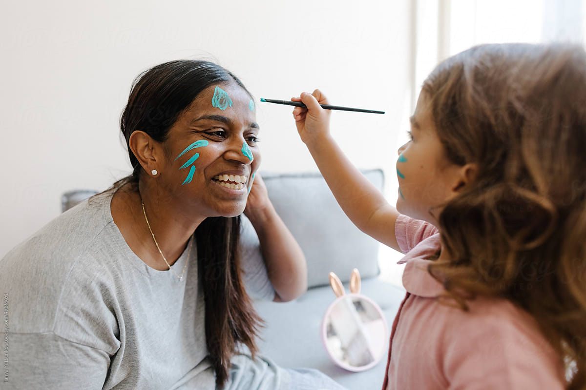 Girl paints her mother\'s face with blue paint