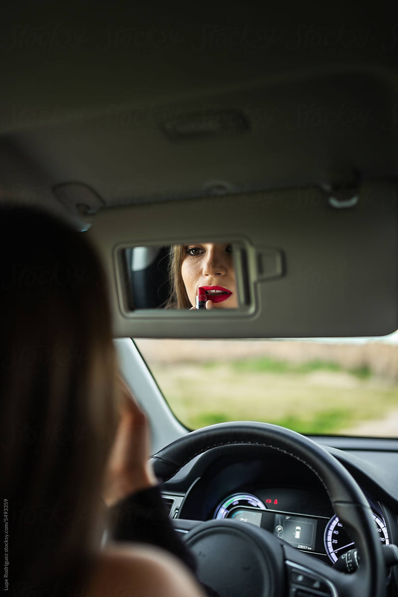 young woman putting on makeup inside a car