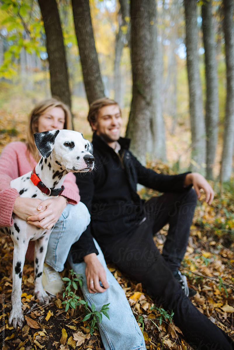 Happy young couple sitting with dog in autumn park