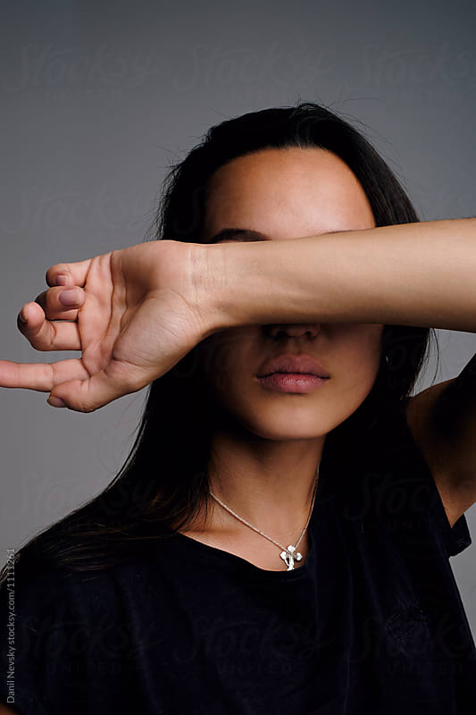 Black-haired woman hiding eyes with arm