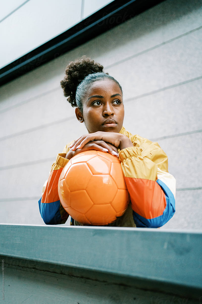 Serious female footballer standing with ball in street