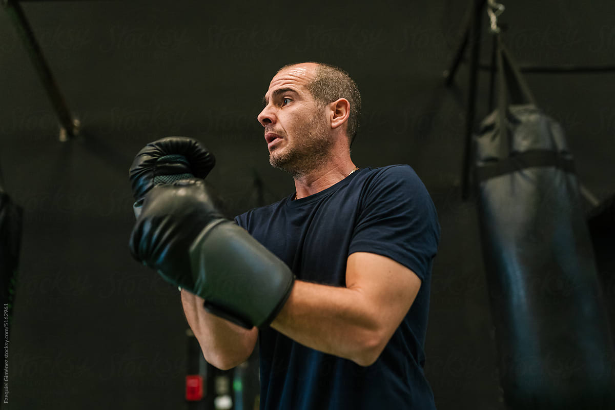 Strong male boxer adjusting gloves near punching bag