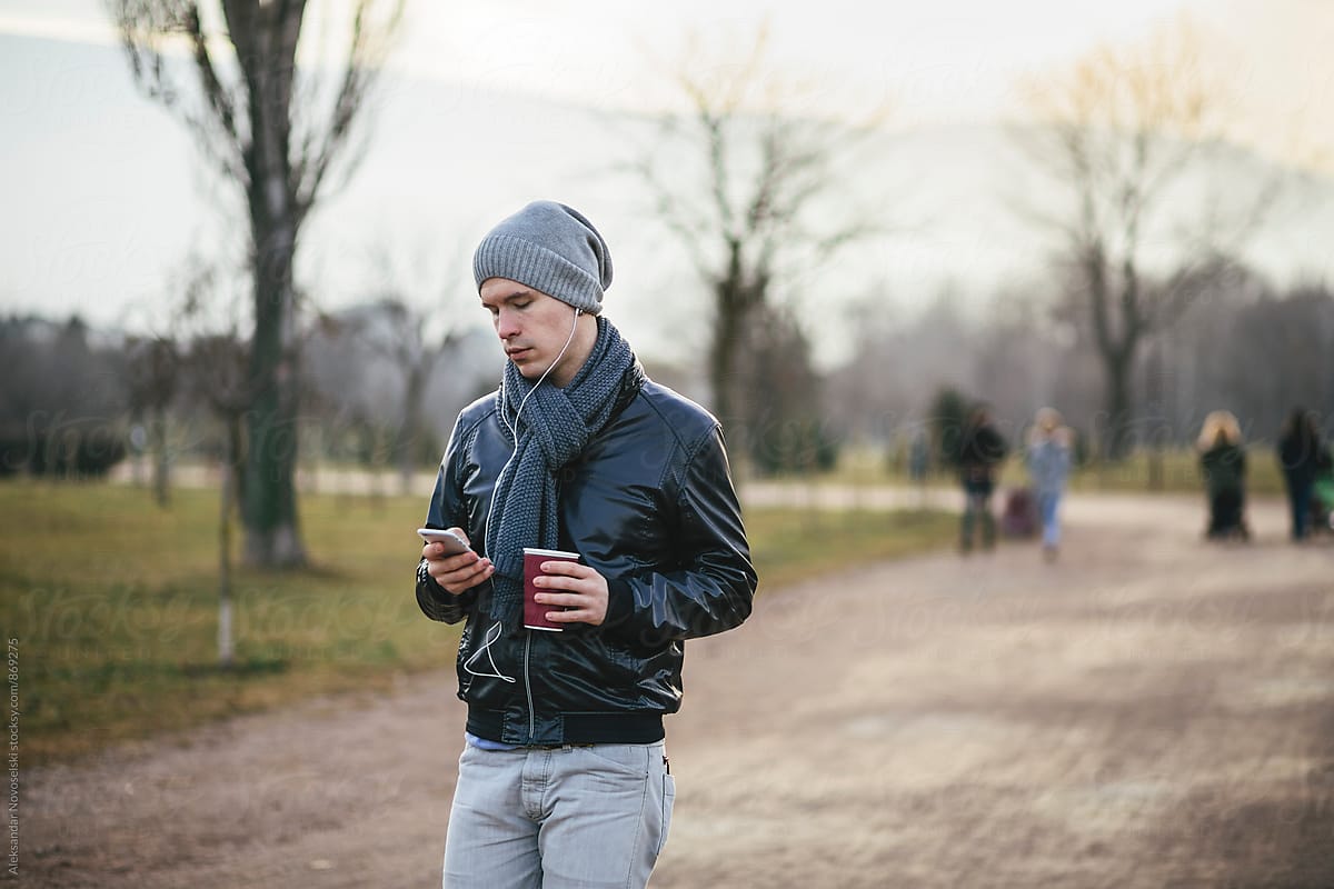 Young man using his smartphone, with headphones plugged in the park