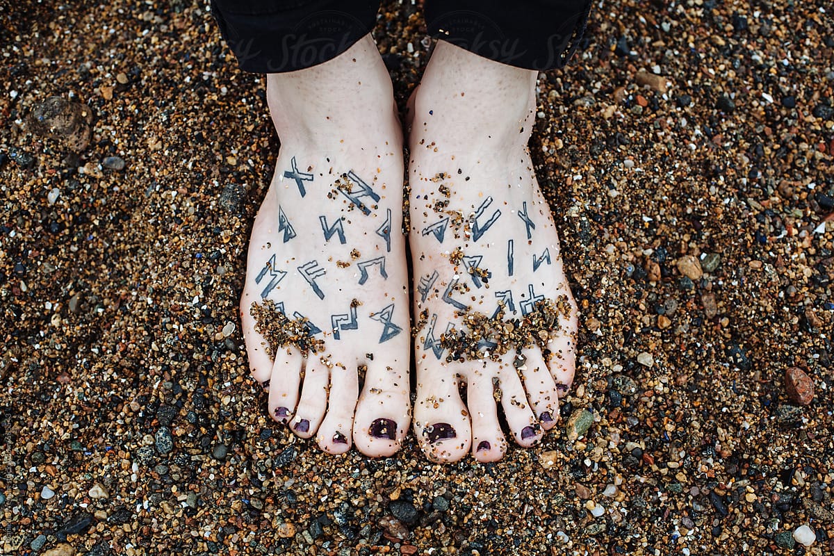 Transgender persons feet with painted nails and runes tattoos