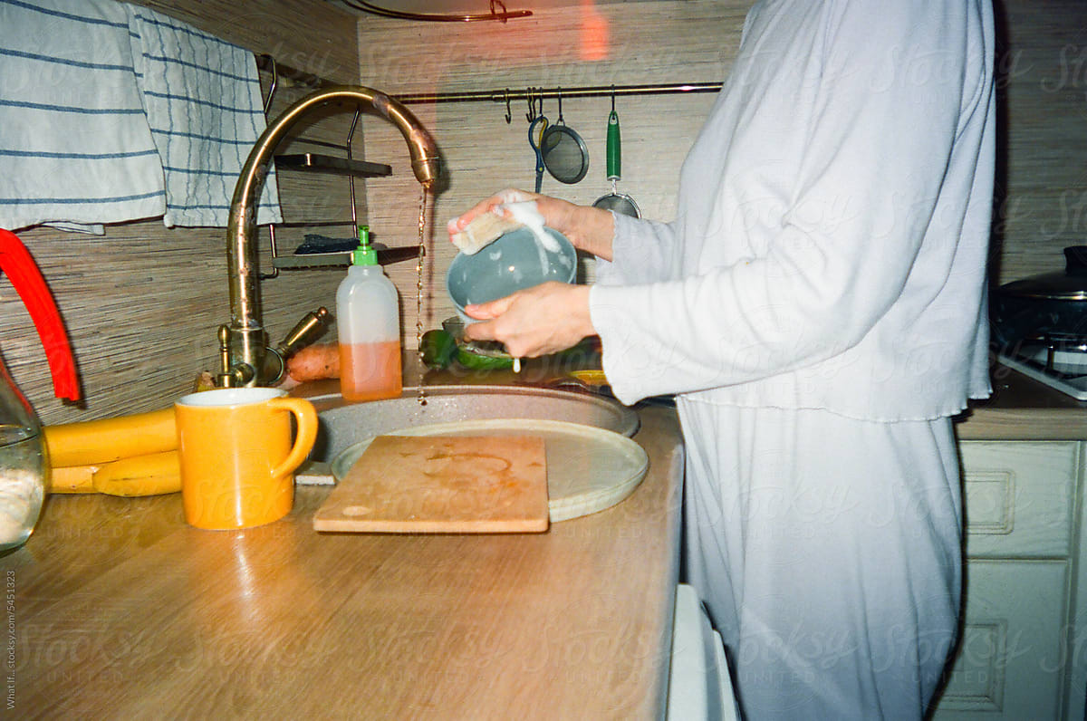 Female washing dishes with her hands in the kitchen.