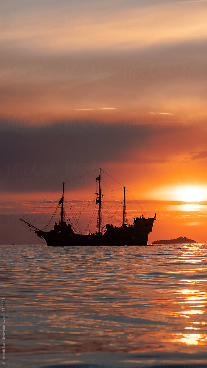 Orange sunset  with\
old historical tall ship (yacht) in sea.